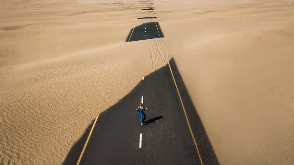 A lone woman walking on a sand-covered road in Dubai's desert, captured from above